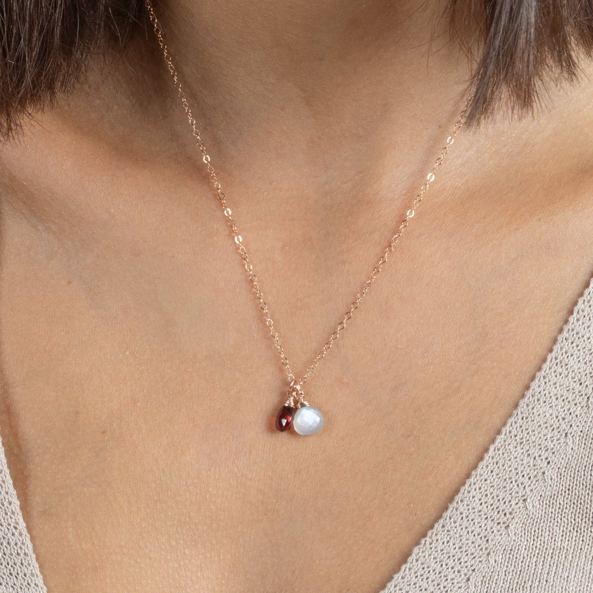 Eine feine Roségold-Kette mit einem grauen Mondstein und einem dunkelroten Granat-Anhänger hängen am Hals des Models.