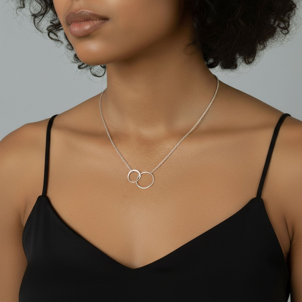 Am Hals des Models hängt eine feine Silberkette mit zwei ineinander verschlungenen Ringen in der Mitte.