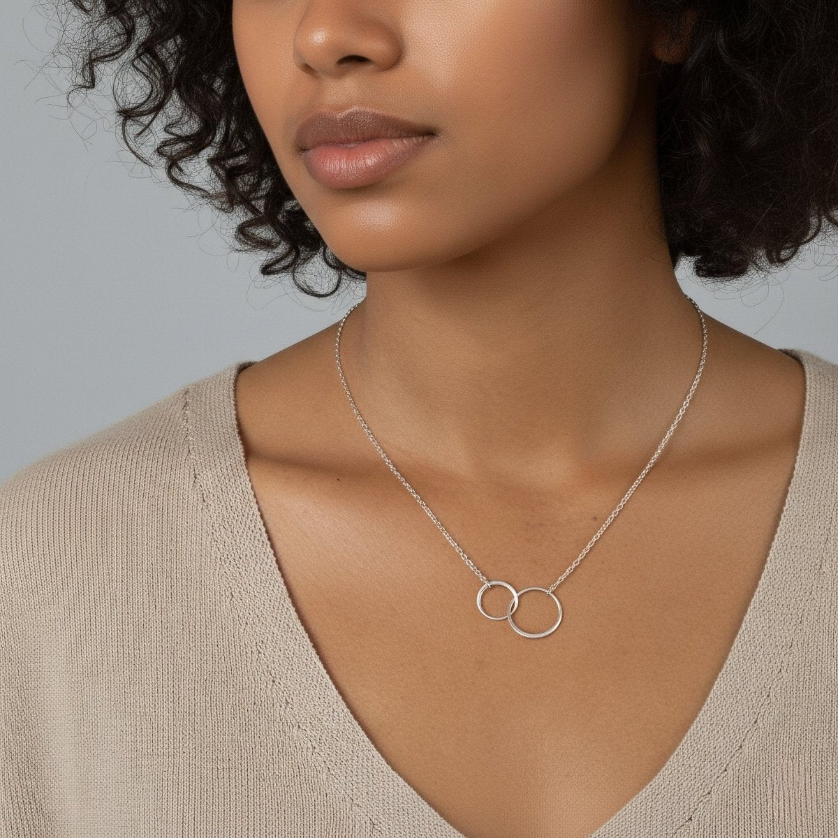 Am Hals des Models hängt eine feine Silberkette mit zwei ineinander verschlungenen Ringen in der Mitte.