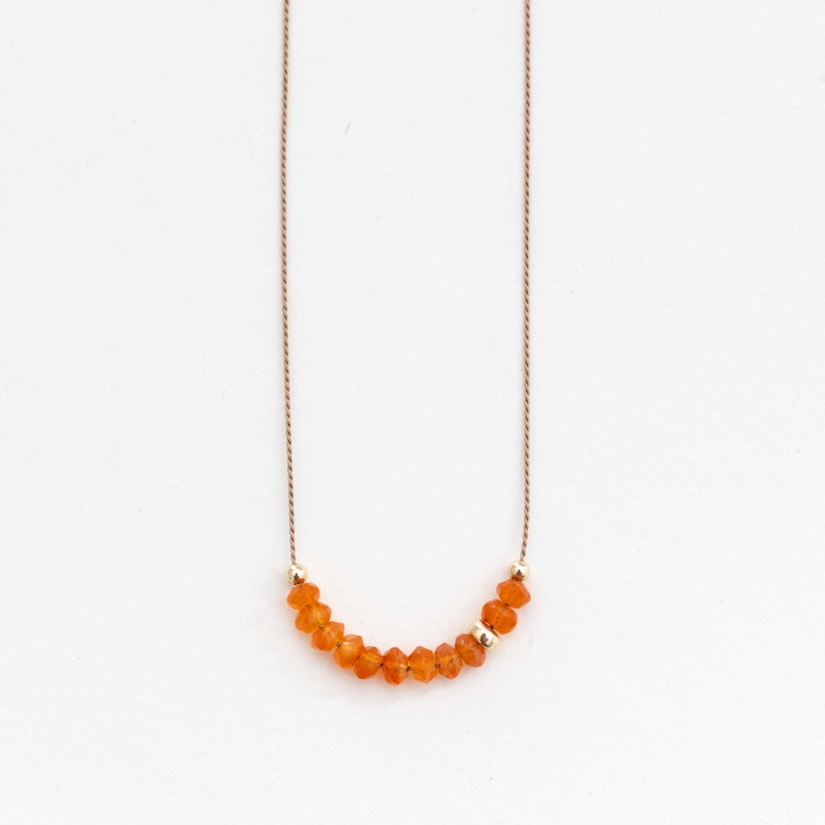 Feine Seidenkette mit orangen Karneol-Rondellen auf weißem Hintergrund.