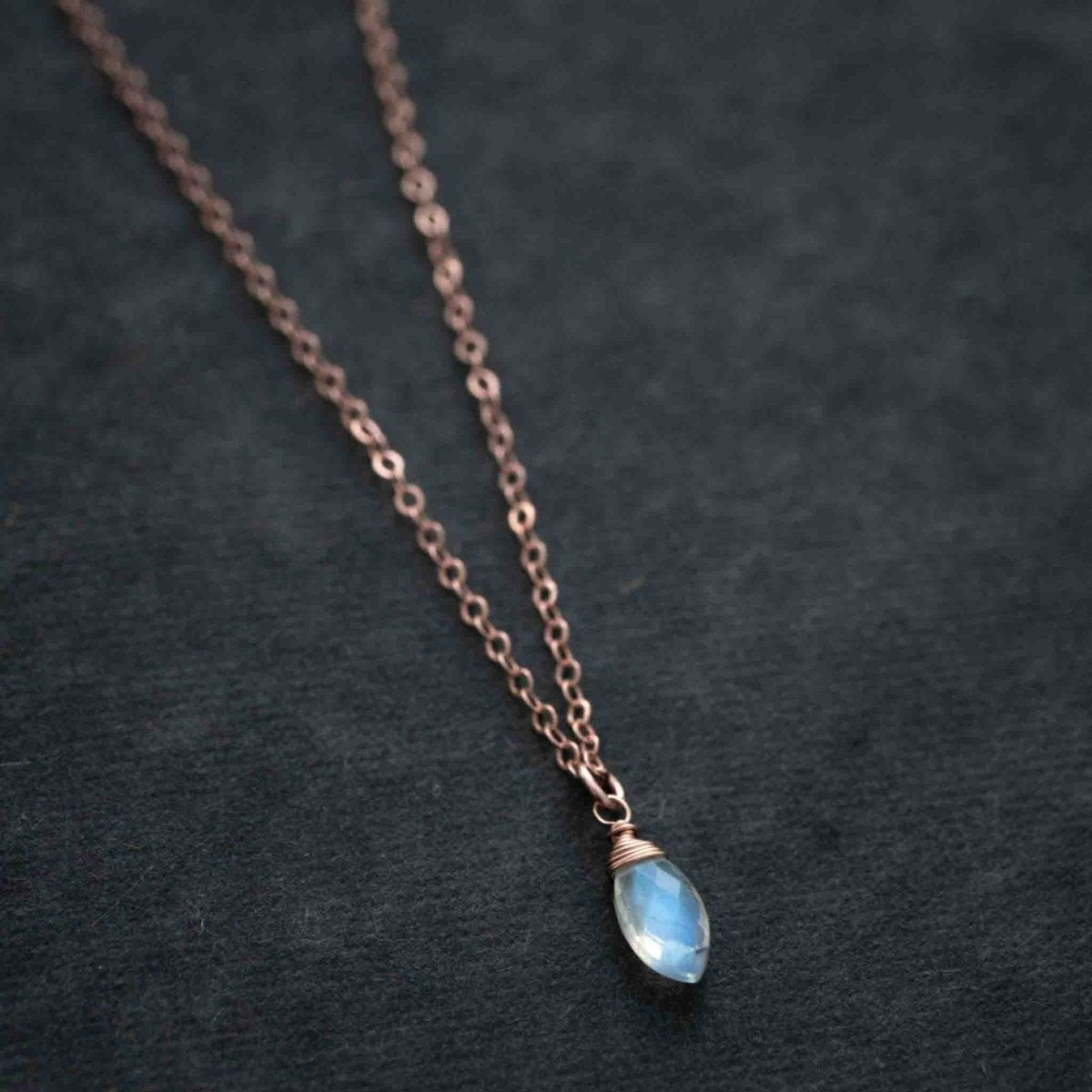 Ein kleiner Mondstein-Anhänger an einer zierlichen Rosé Goldkette liegt auf schwarzem Hintergrund.