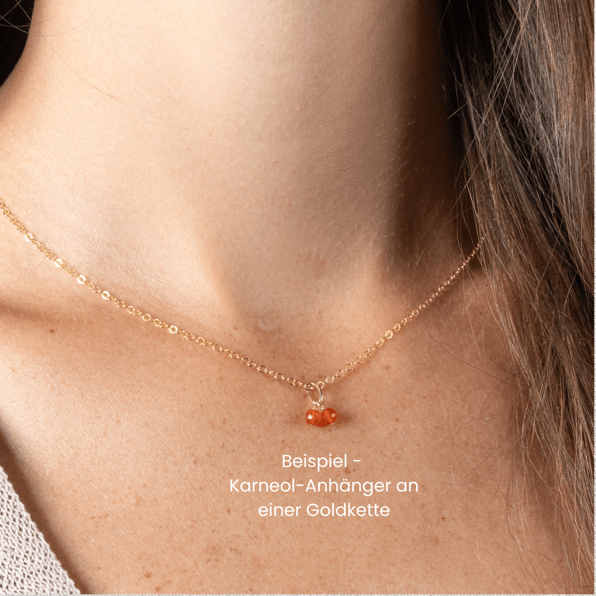 Am Hals des Models hängt eine kurze feine Goldkette mit einem Anhänger, der aus zwei kleinen Karneolen besteht. Darunter steht auf Deutsch: Beispiel - Karneol-Anhänger an einer Goldkette.