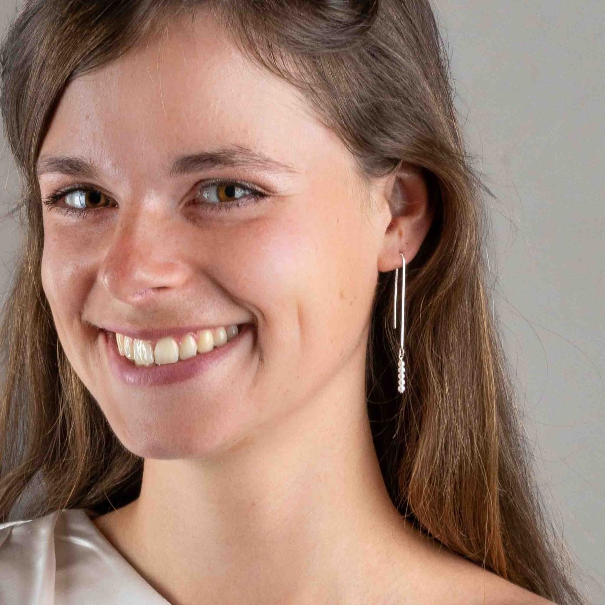 Am Ohr des Models hängt ein silberner Einfädler-Ohrring mit einer Reihe weißer Perlen.