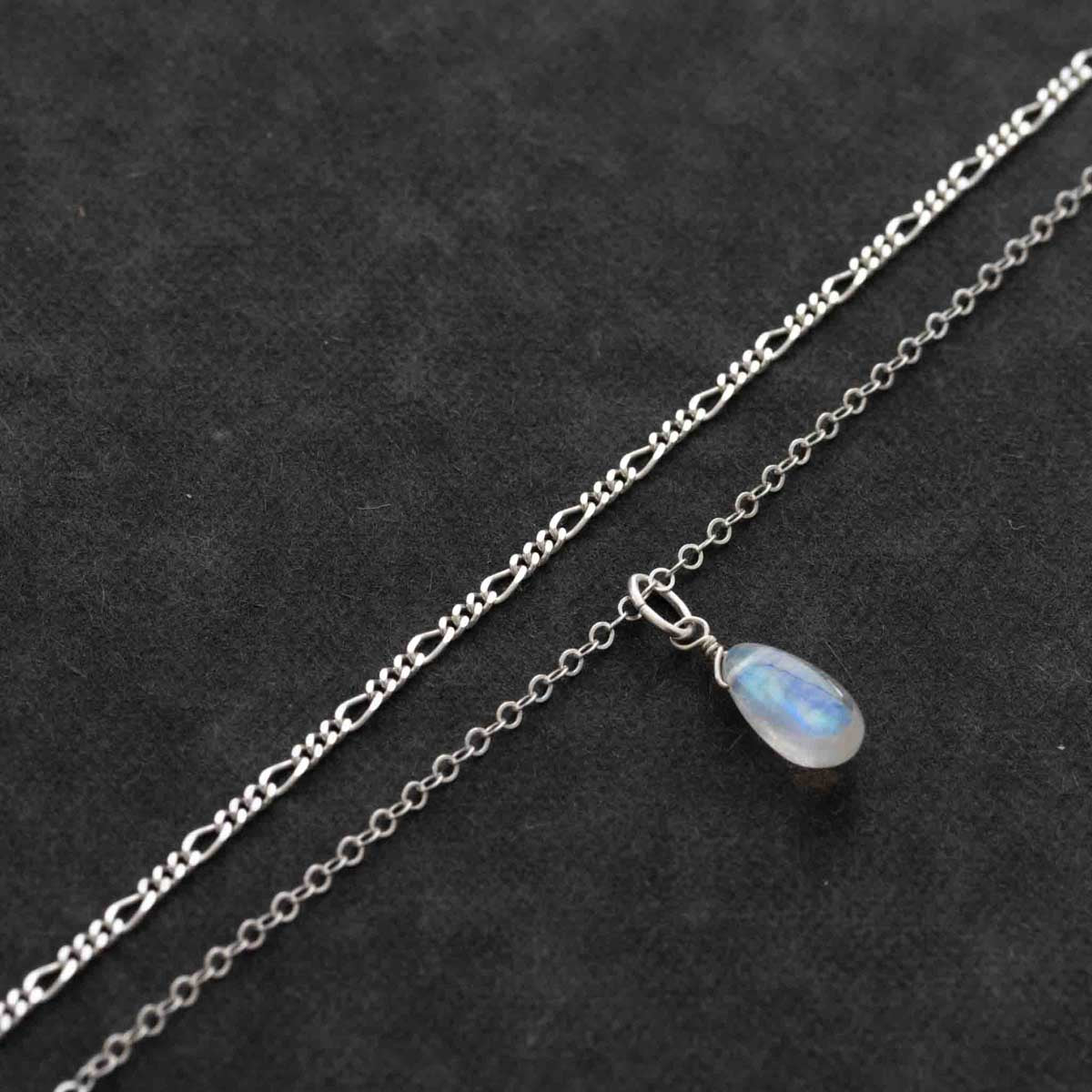 Detailaufnahme eines silbernen Kettensets, bestehend aus einer Figaro-Kette und einer Ankerkette mit Mondstein-Anhänger.