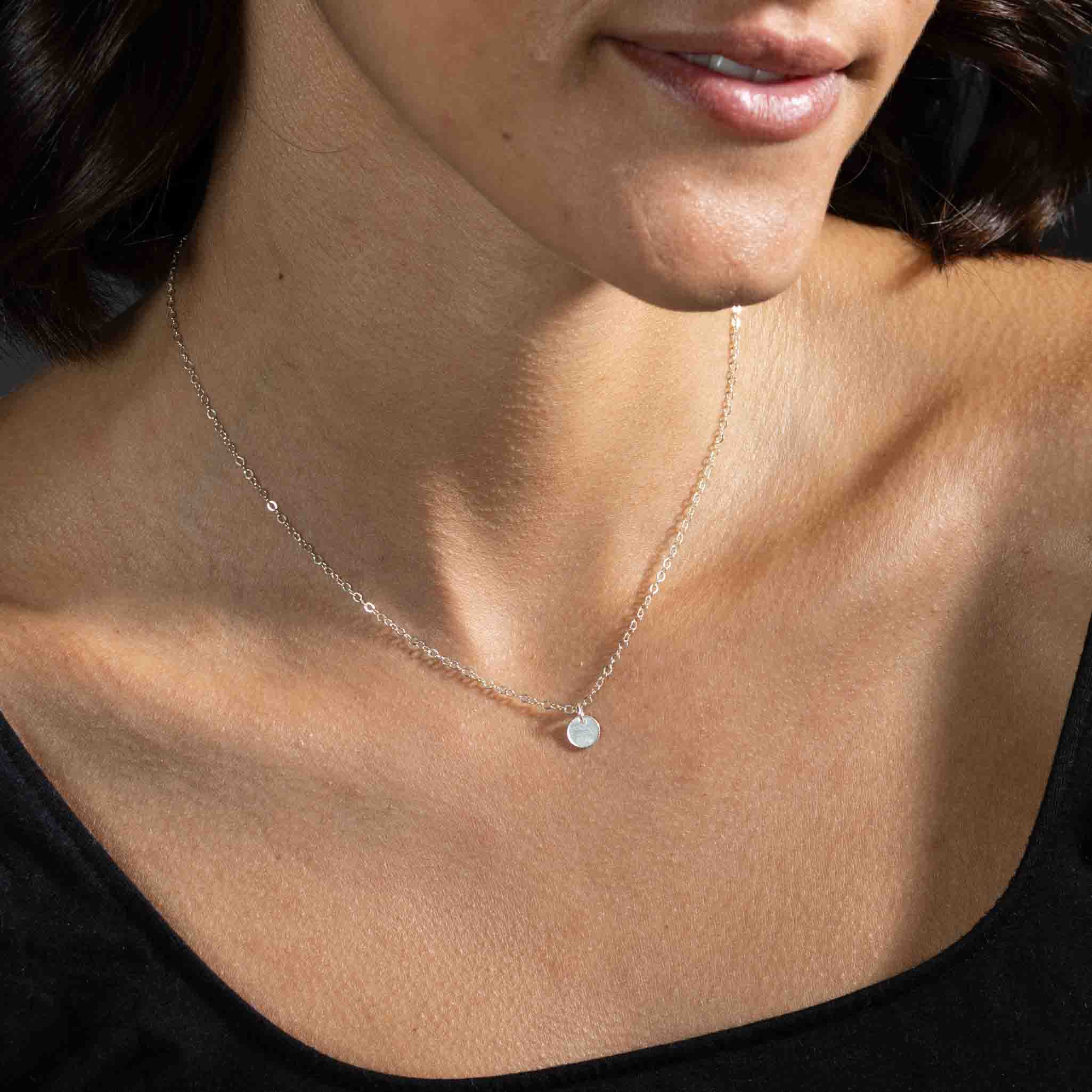 Am Hals des Models hängt eine kurze, feine Ankerkette aus 925 Silber mit einem kleinen, runden Plättchenanhänger, der silbern glänzt.