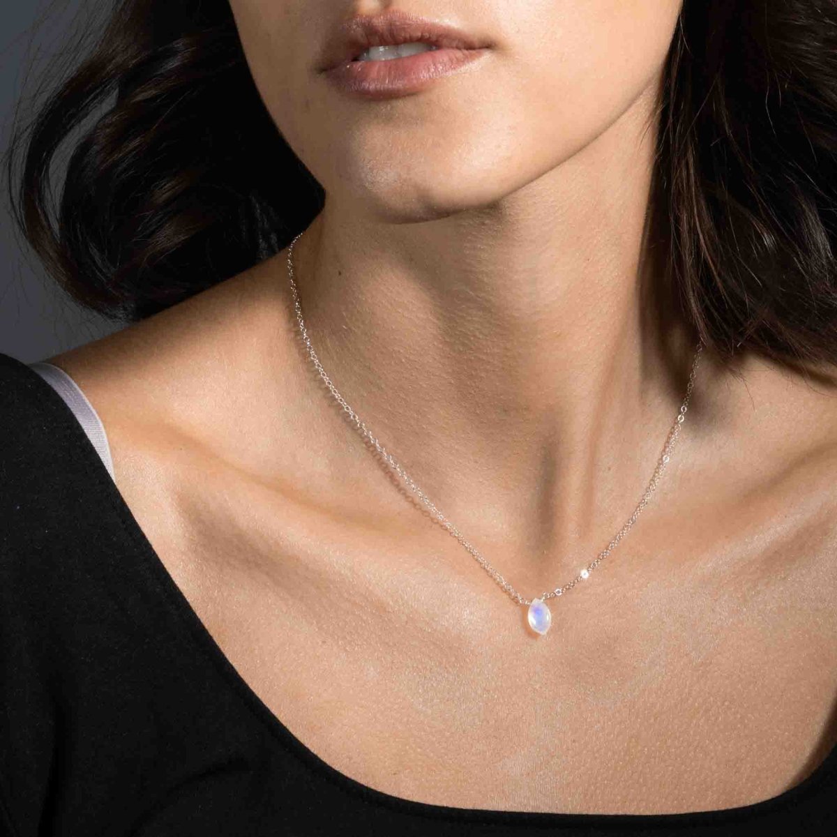 Ein bläulich schimmernder Mondstein ist als Verbinder in eine feine Halskette aus 925 Silber eingearbeitet. Die Kette hängt am Hals des Models.