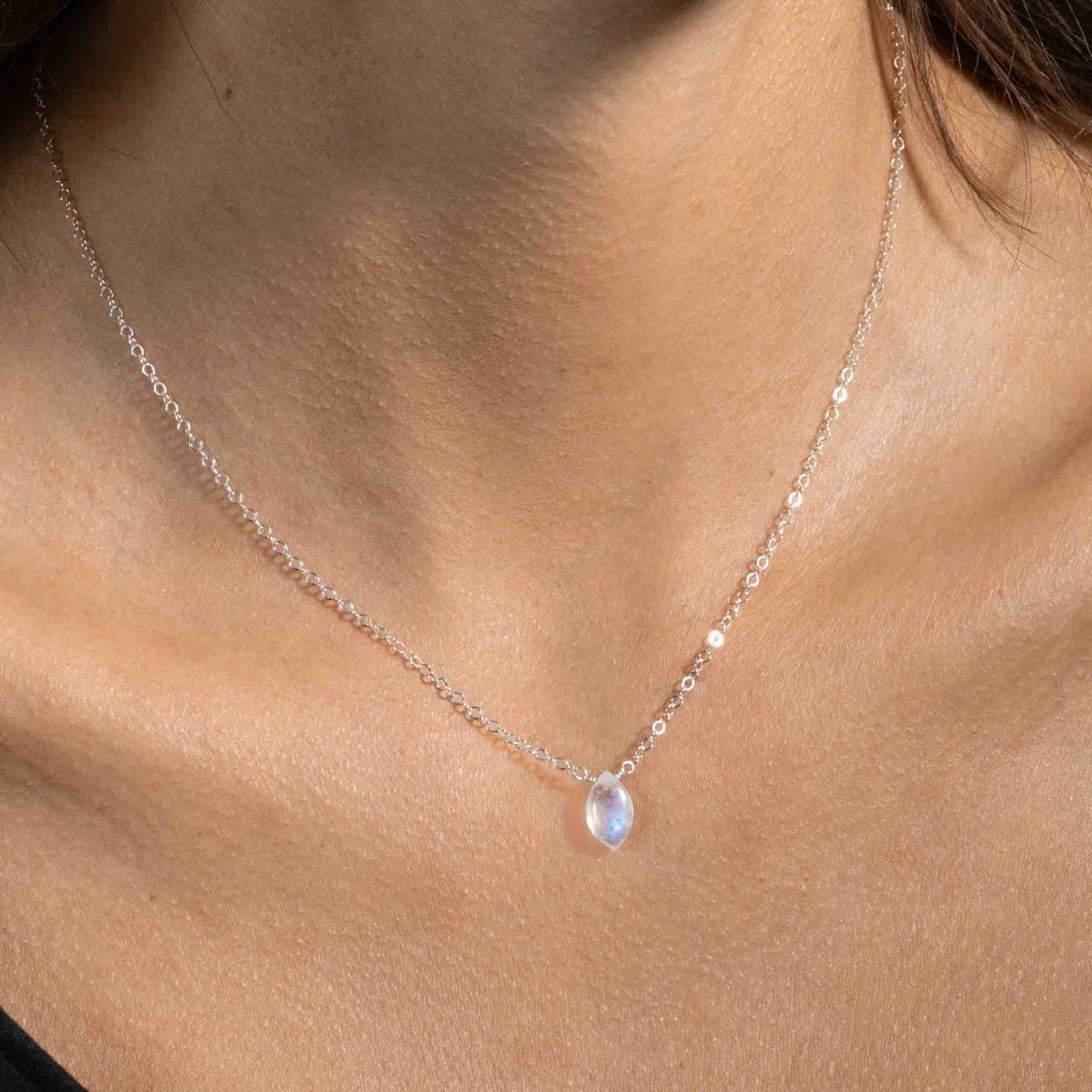 Ein bläulich schimmernder Mondstein ist als Verbinder in eine feine Halskette aus 925 Silber eingearbeitet. Die Kette hängt am Hals des Models.
