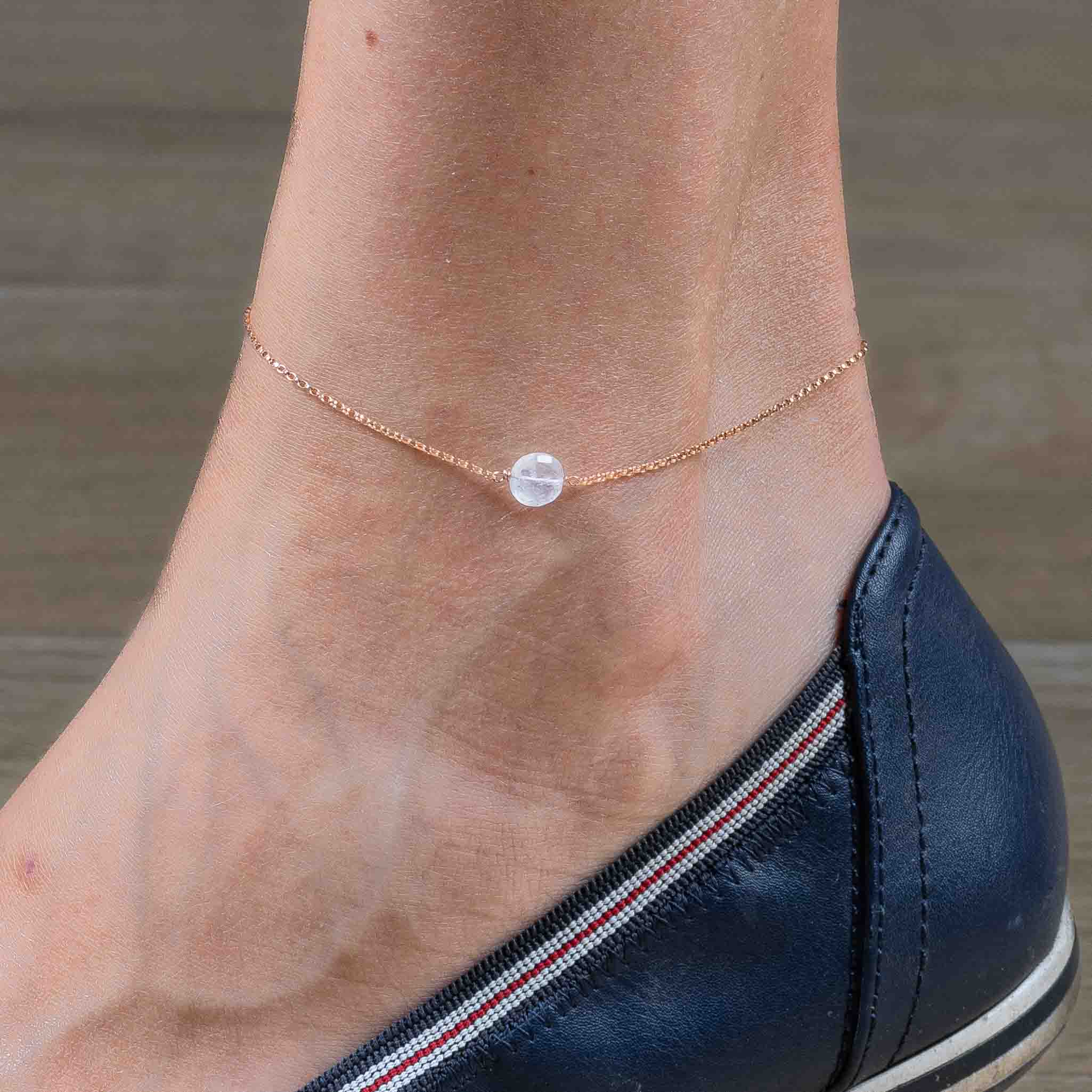 Ein rosé goldenes Fußkettchen mit einem Mondstein am Fußgelenk des Models.