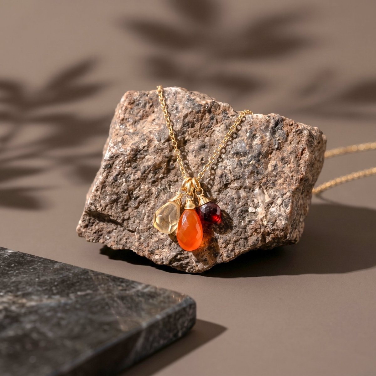 Zierliche Goldkette mit Citrin-, Karneol- und Granat-Anhänger von Deko-Stein hängend.
