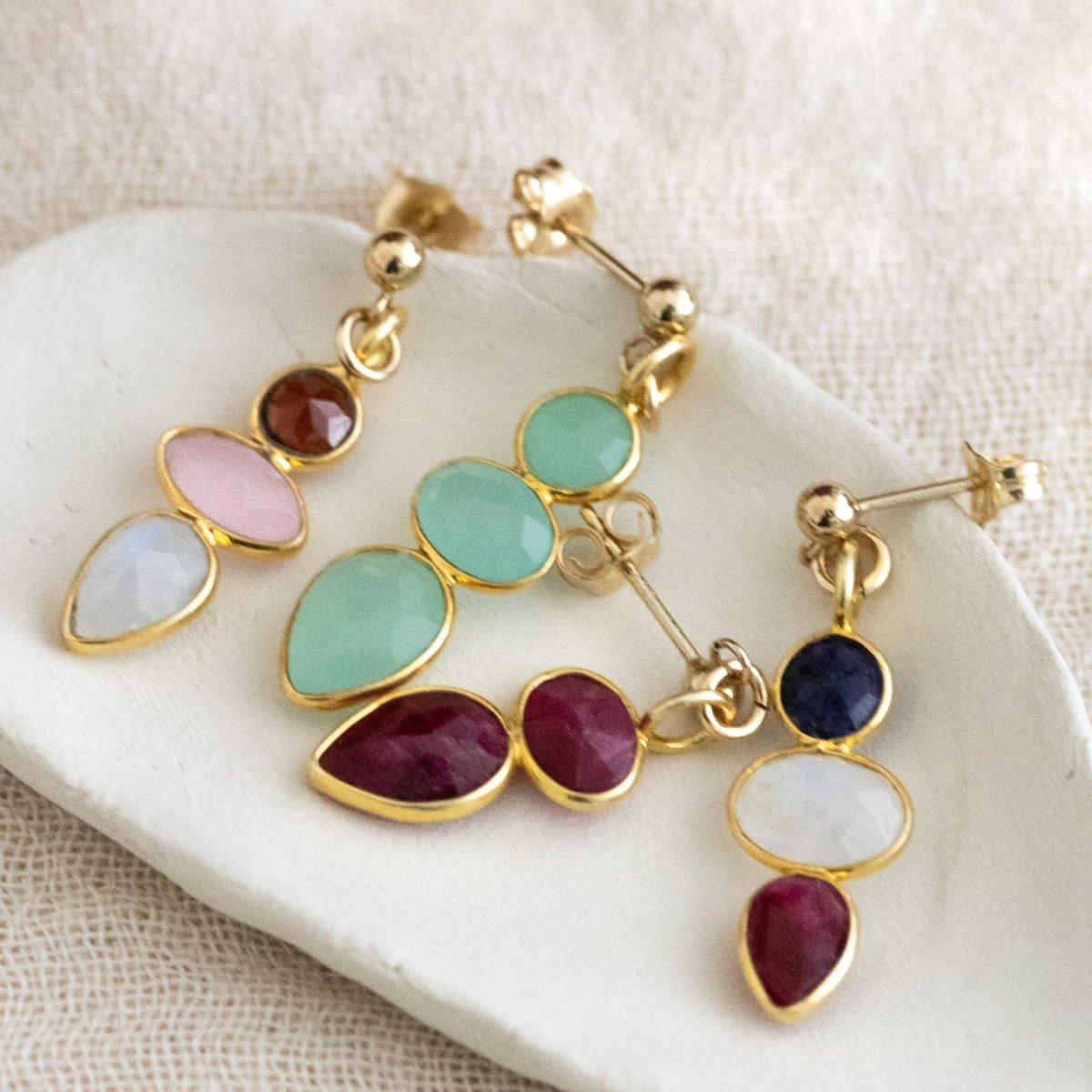 Vier unterschiedliche bunte Ohrringe mit kleinen Edelsteinen liegen in einem weißen Schälchen.