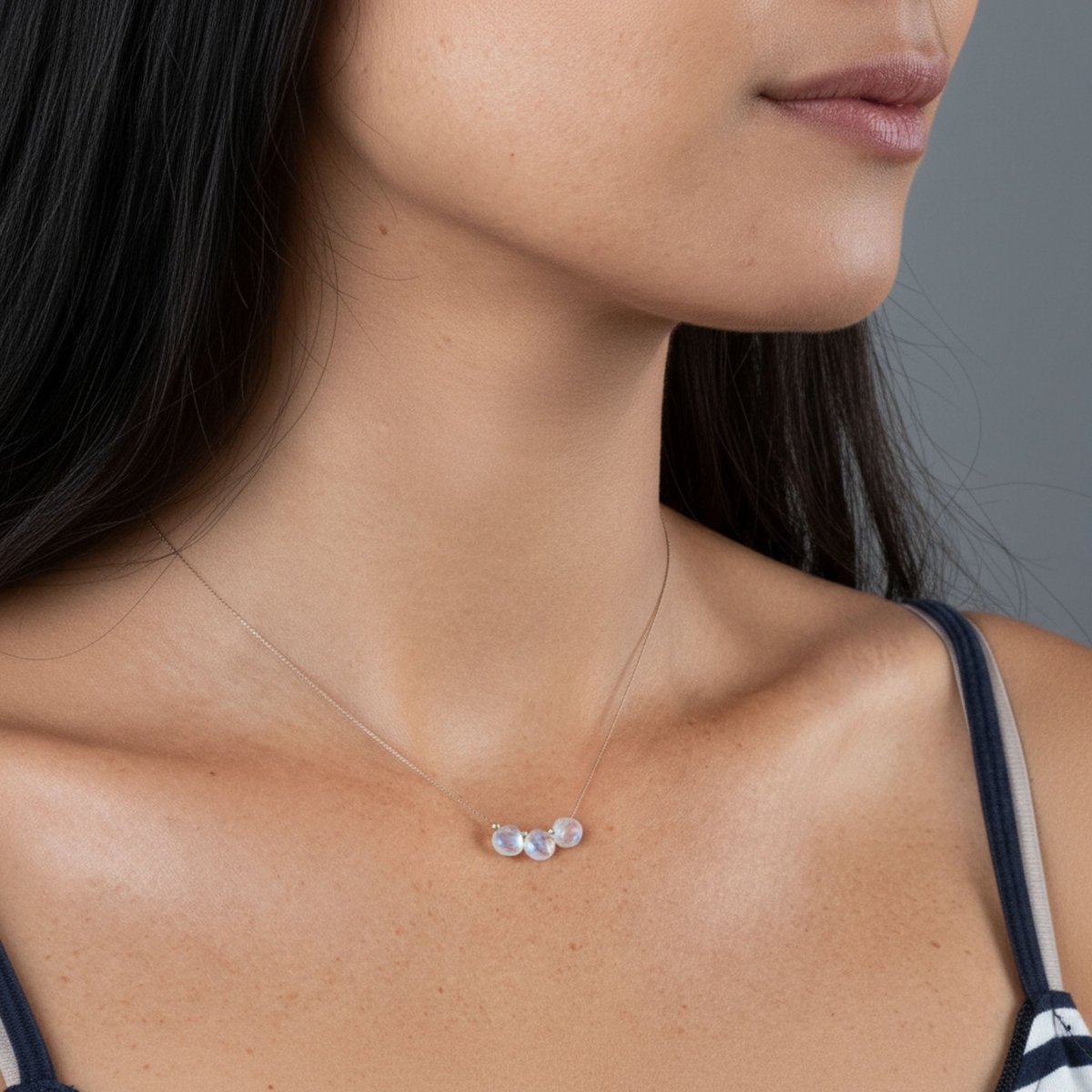 Eine dünne Seidenkette mit drei aufgezogenen Mondsteinen hängt am Hals des Models.