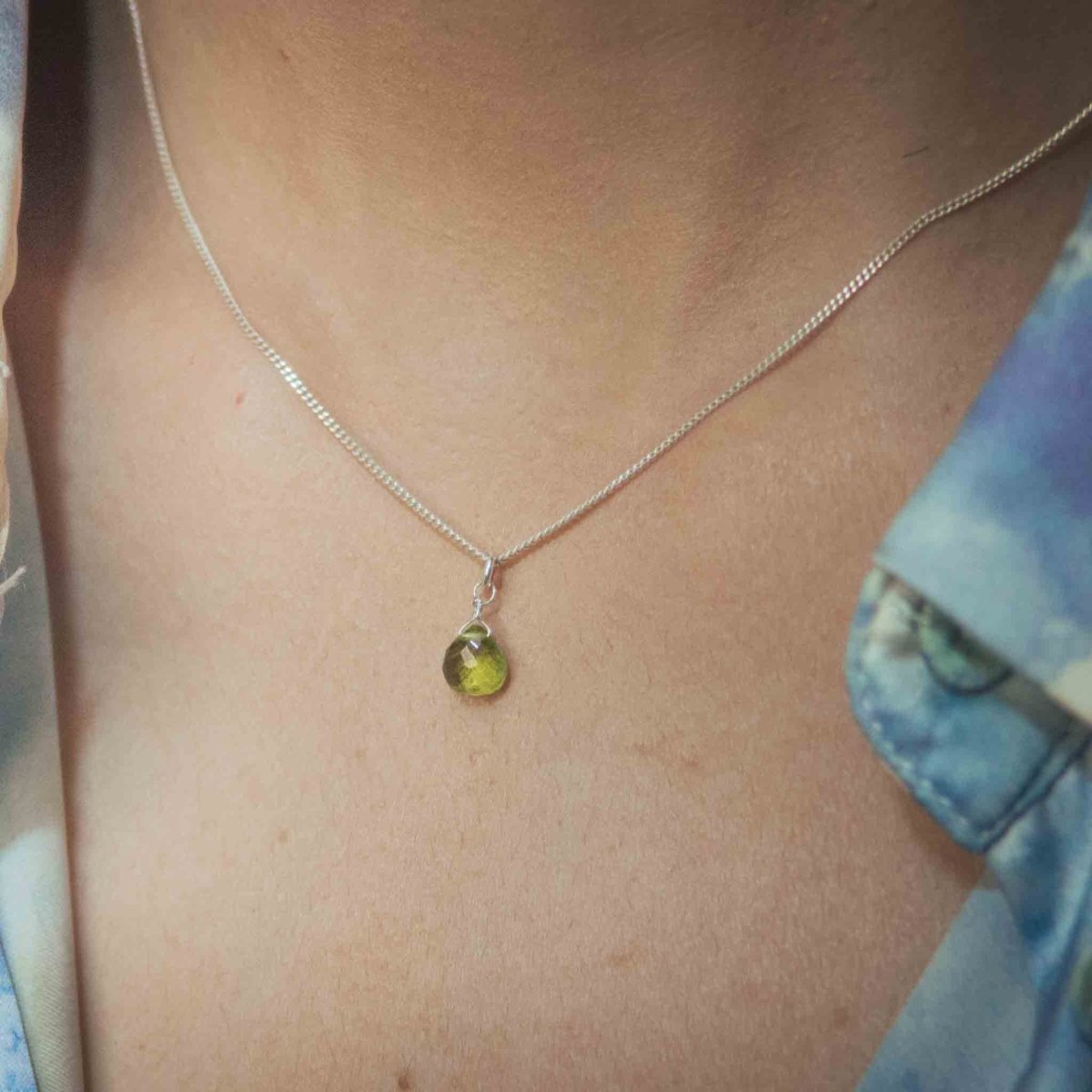 Am Hals des Models hängt eine kurze Silberkette mit einem kleinen, grünen Peridot-Anhänger.