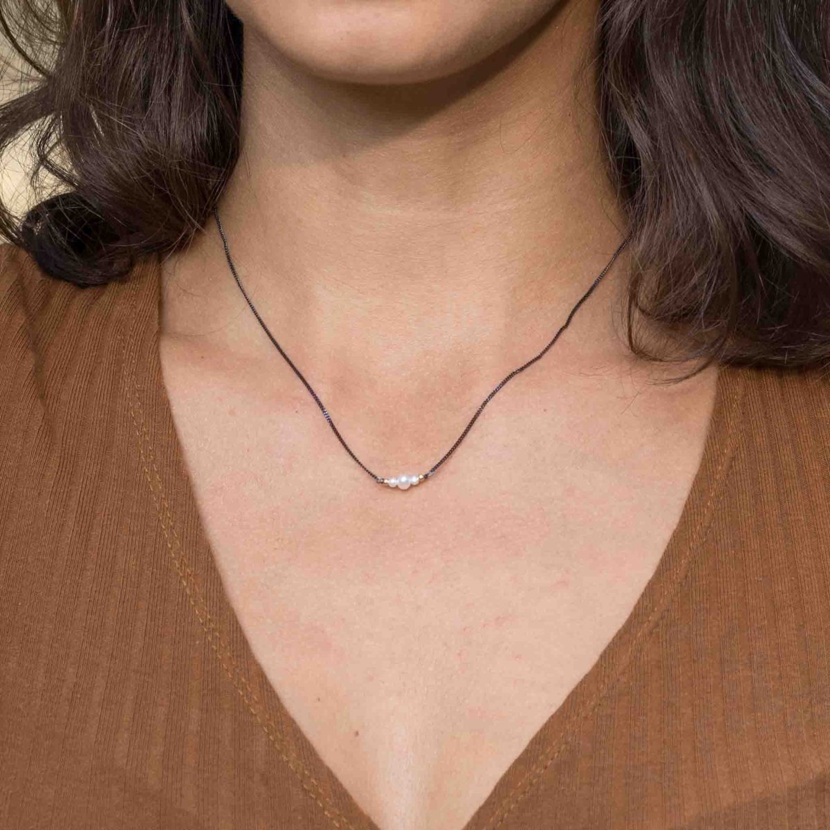 Am Hals des Models hängt eine schwarze Silberkette mit drei weißen Perlen in der Mitte.