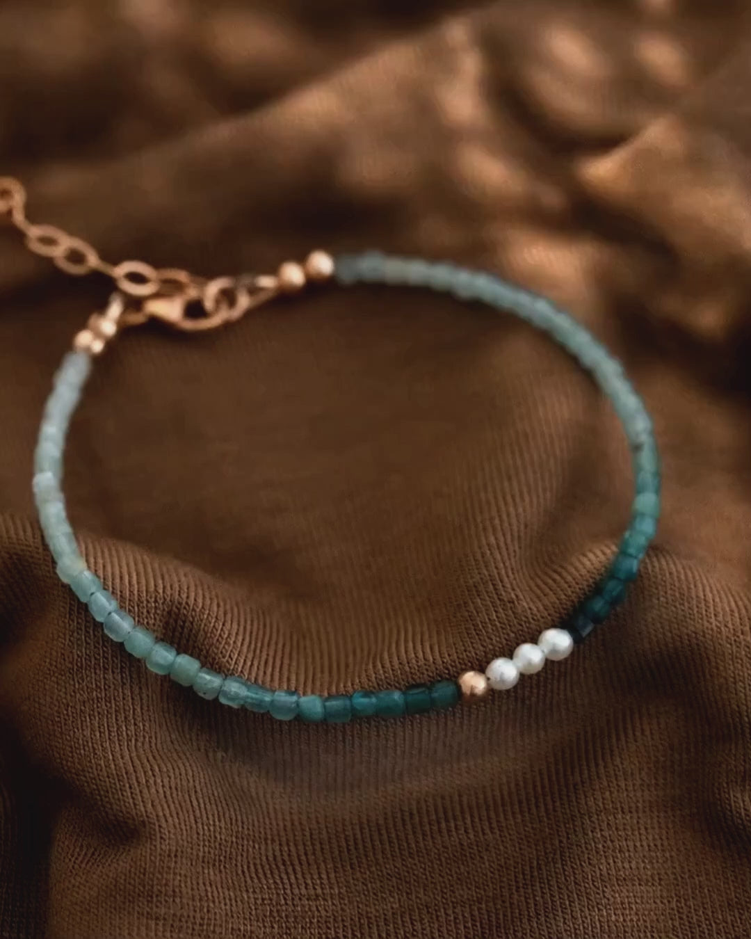 Verschiedene Fotos und kurze Animationen zeigen ein filigranes Grandidierit-Armband mit weißen Süßwasserperlen.