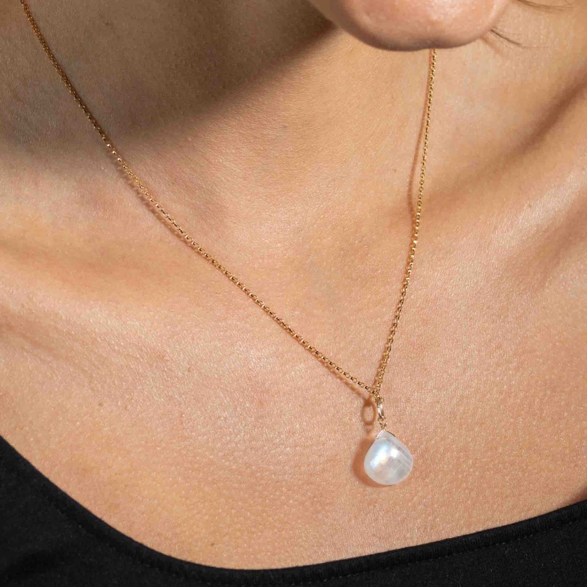 Am Hals des Models hängt eine Goldkette mit einem bläulich schimmernden Mondstein-Anhänger.