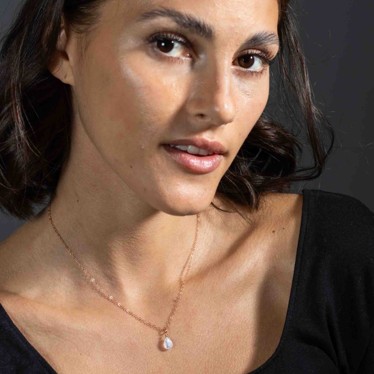 Eine feine rosé goldene Halskette mit einem bläulich schimmernden Mondstein-Anhänger hängt am Hals des Models.
