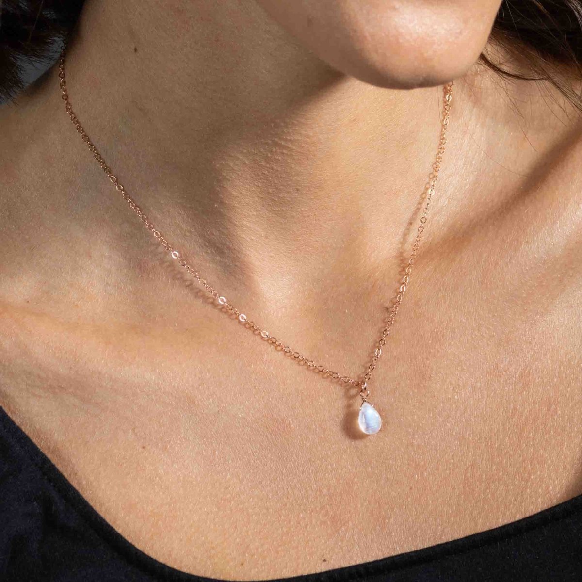 Eine feine rosé goldene Halskette mit einem bläulich schimmernden Mondstein-Anhänger hängt am Hals des Models.