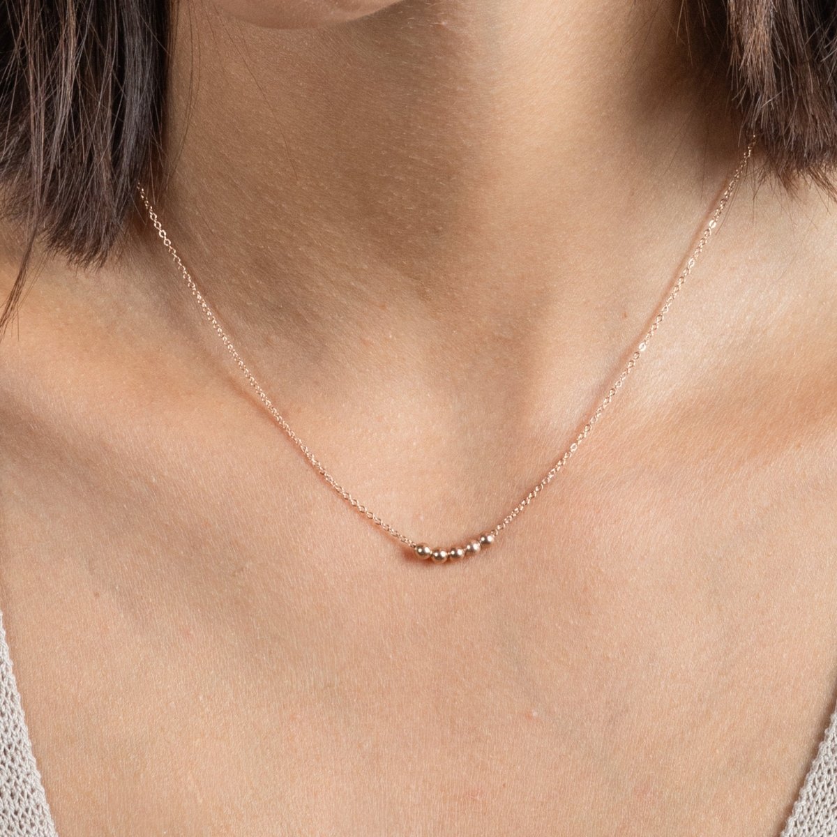 Am Hals des Models hängt eine kurze Roségold-Kette mit fünf aufgezogenen kleinen Rosegold-Perlen in der Mitte.