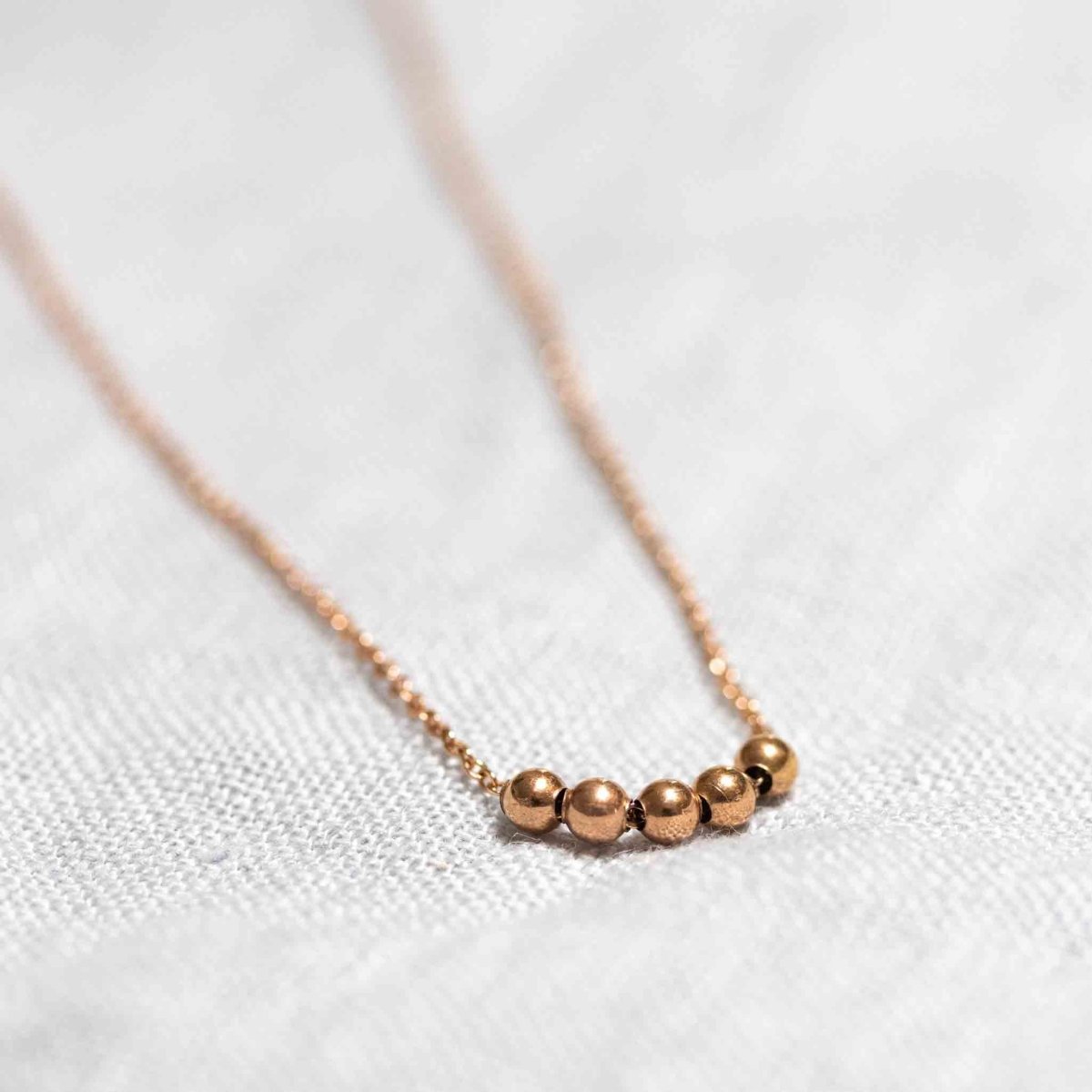 Eine feine Rosé Goldfill-Kette mit fünf kleinen Rosegold-Perlen auf weißem Hintergrund.