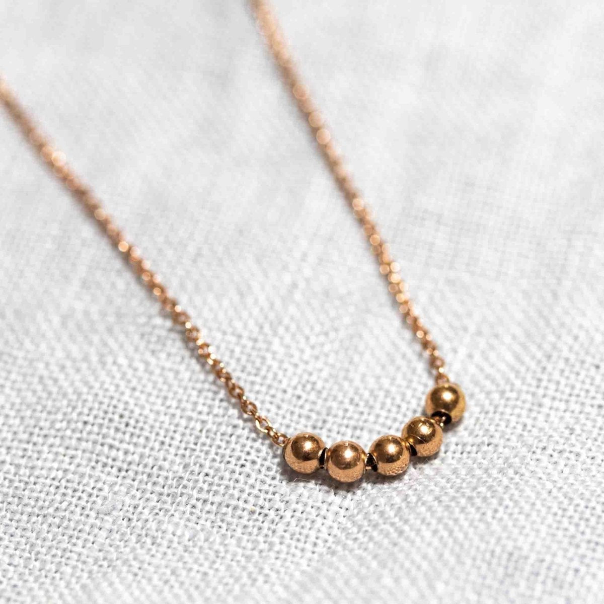Eine feine Rosé Goldfill-Kette mit fünf kleinen Rosegold-Perlen auf weißem Hintergrund.