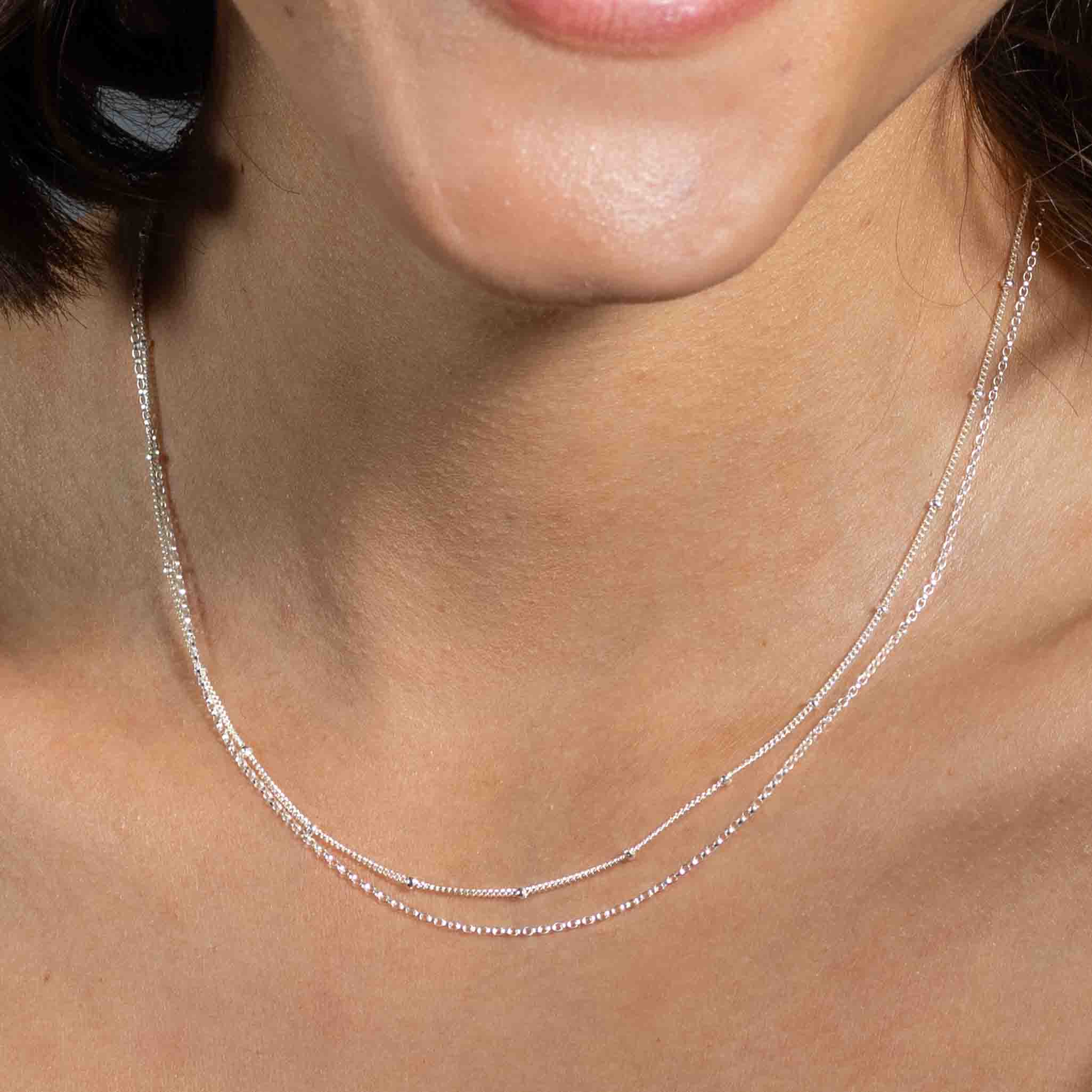 Am Hals des Models hängt eine kurze, doppelreihige Silberkette. 