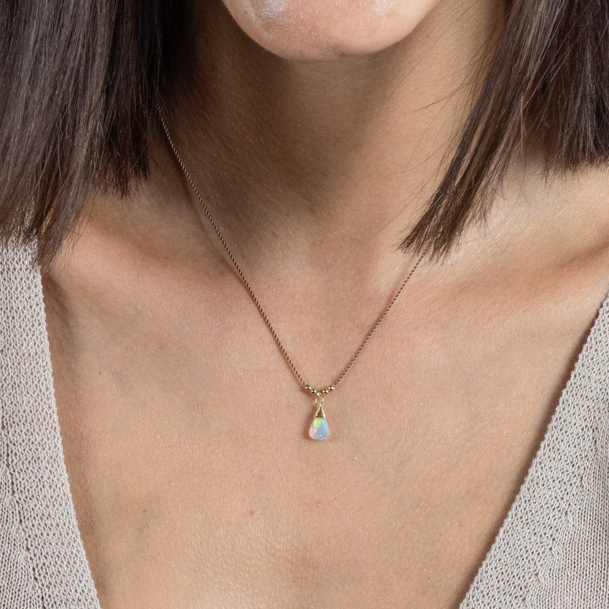 Eine dünne, braune Schnurkette mit einem dreieckigen Opal-Anhänger und goldenen Akzenten hängt am Hals des Models.