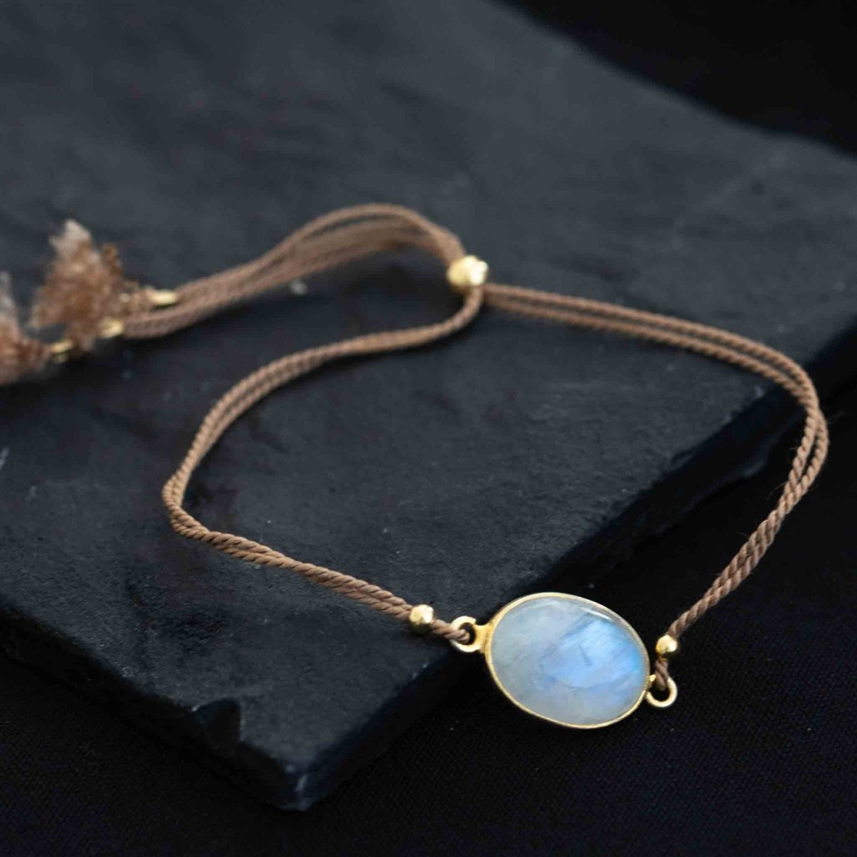 Ein beiges Seidenarmband mit einem ovalen, gold gefassten Mondstein in der Mitte.