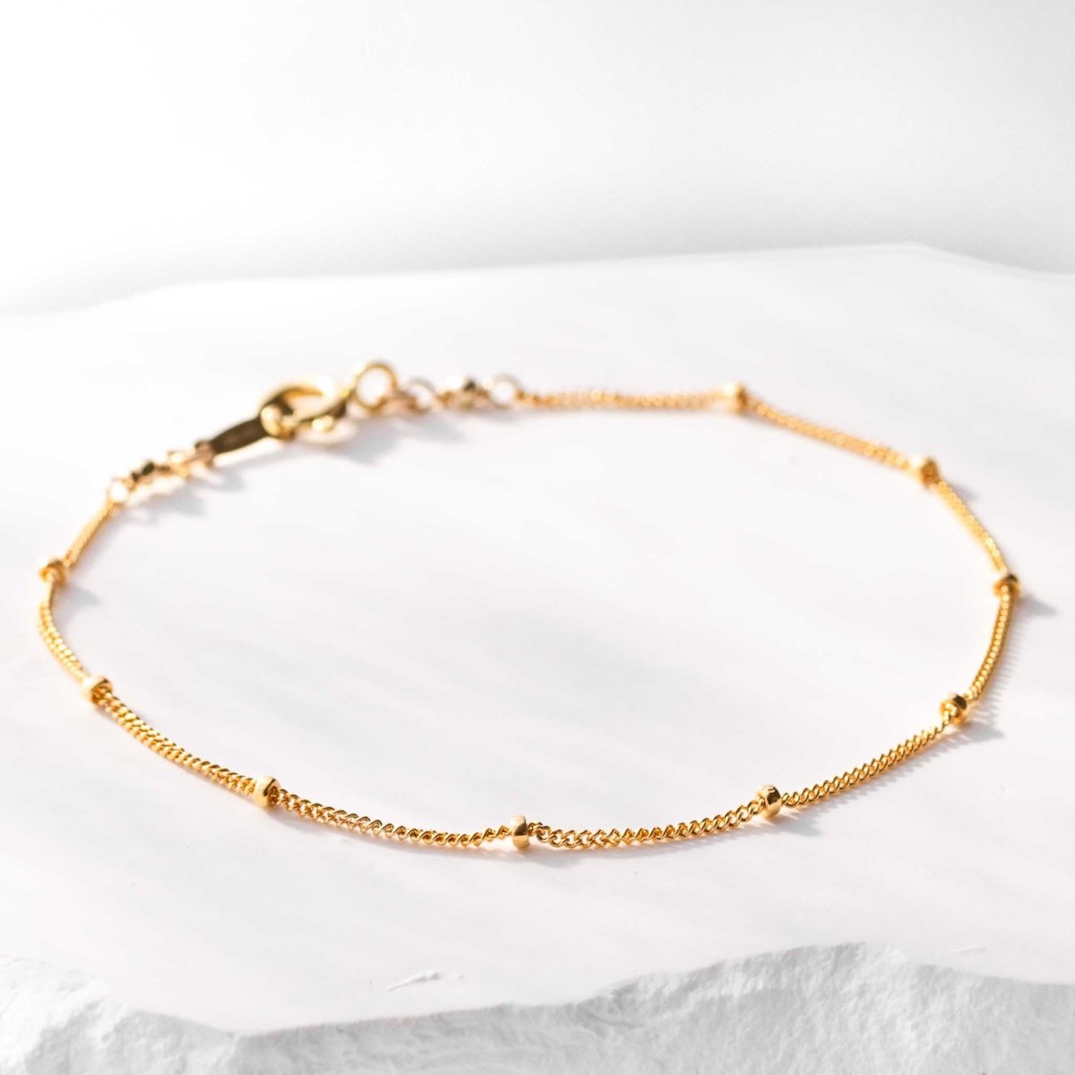 Dünnes, goldenes Armband aus einer Panzerkette mit kleinen, goldenen Perlen auf weißem Hintergrund.