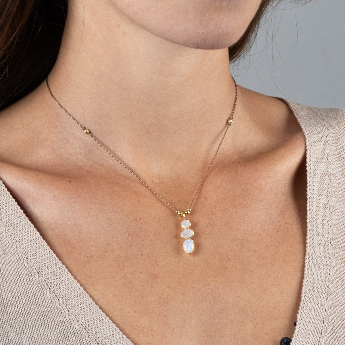 Eine kurze Schnurkette mit einem länglichen Anhänger, der aus drei übereinander in gold gefassten Mondsteinen besteht, hängt am Hals des Models.