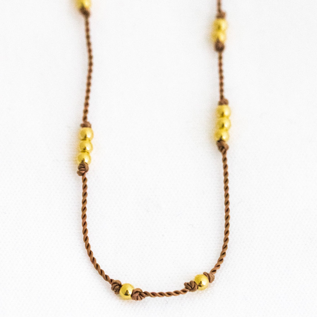 Dünne, beige Kordelkette mit unregelmäßig verteilten Goldperlen in der Nahansicht.