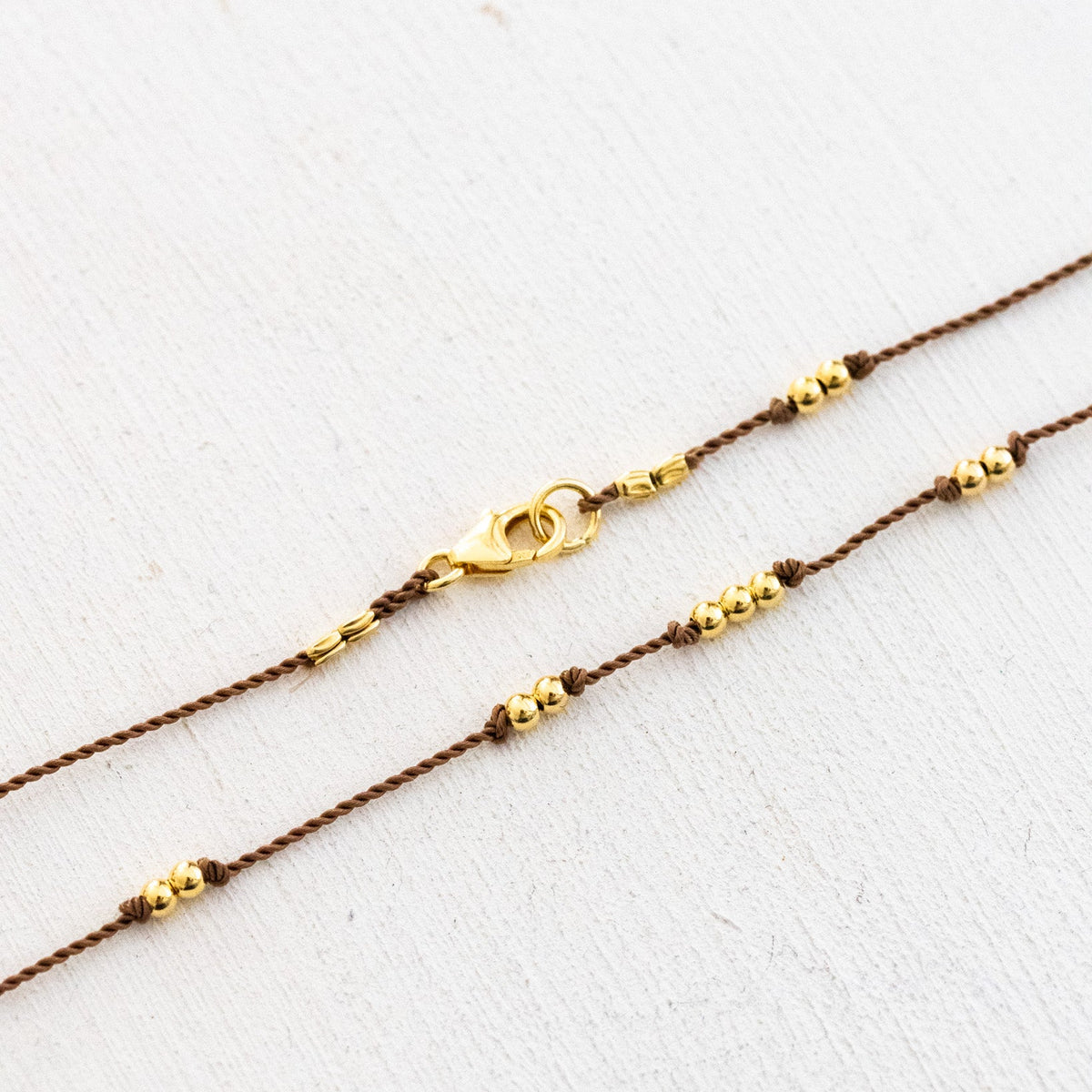 Beige Kordelkette mit unregelmäßig verteilten Goldperlen in der Detail-Ansicht mit Karabiner-Verschluss.