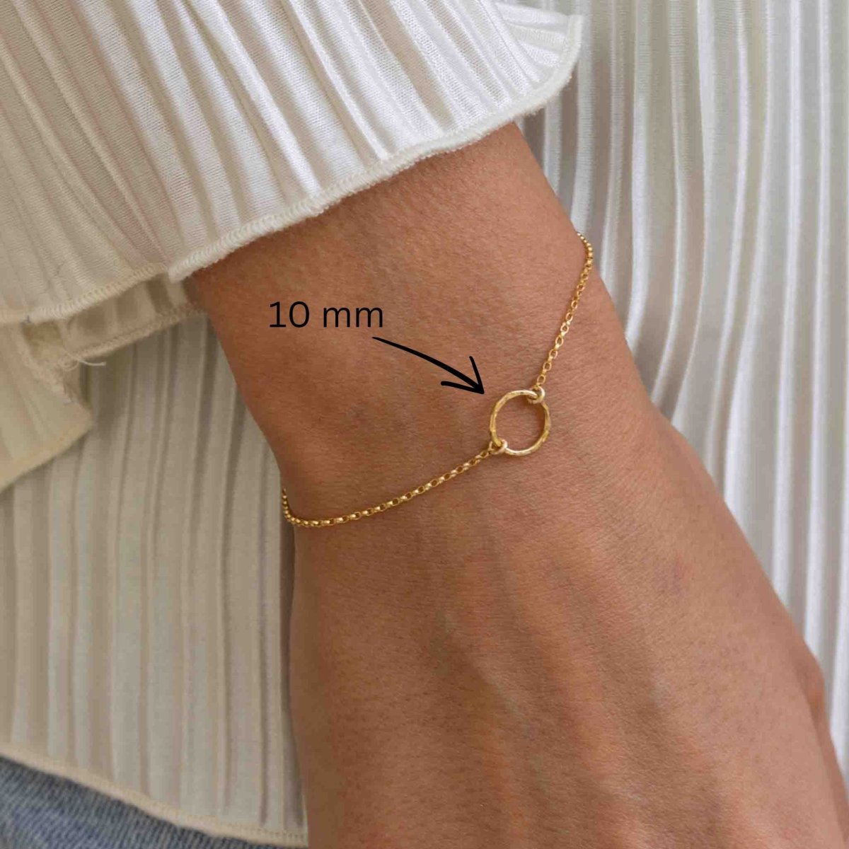 Das Model trägt am Handgelenk ein dünnes, goldenes Armband mit einem 10 mm großen, gehämmerten Ring im Zentrum.