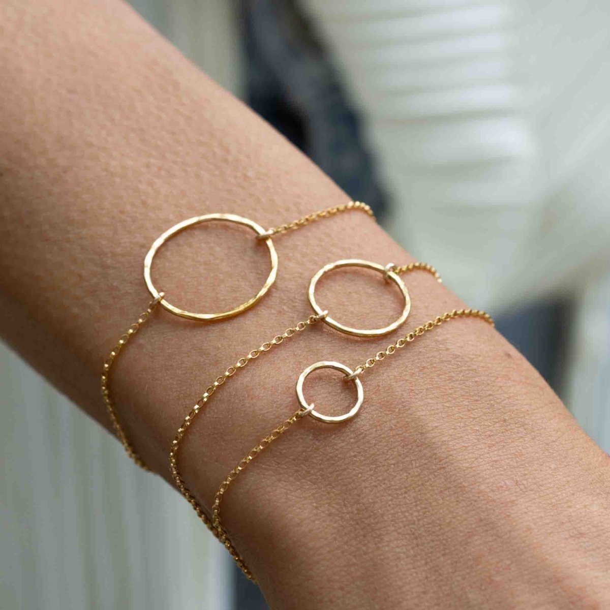 Das Model trägt am Handgelenk drei goldene Armbänder. Jedes Armband hat einen offenen Ring in der Mitte, jeweils unterschiedlicher Größe.