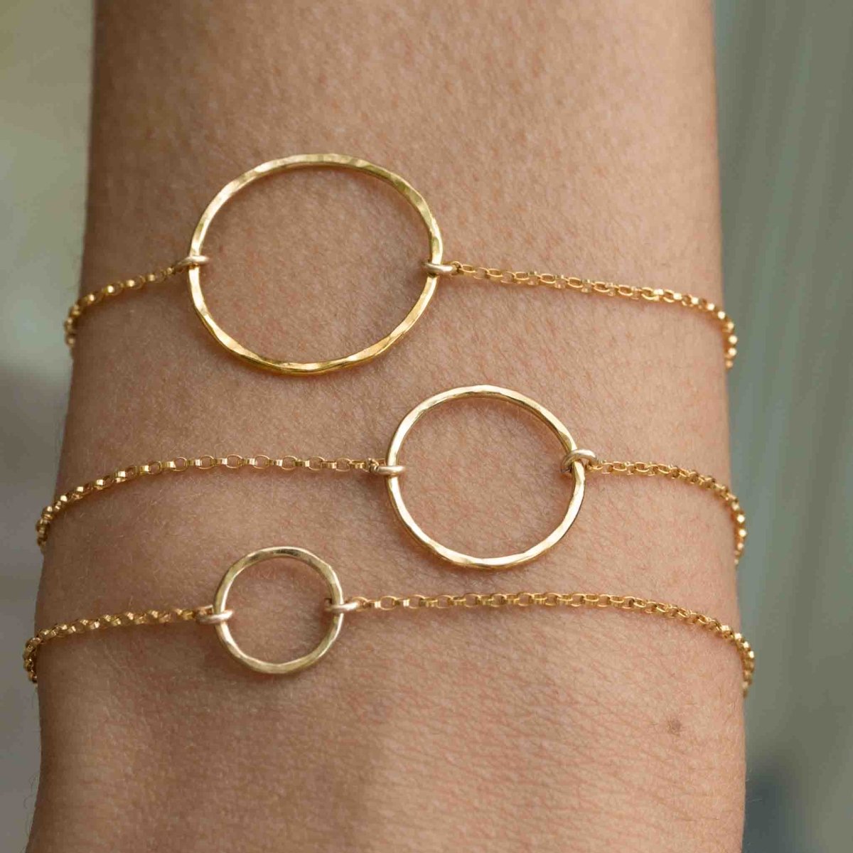 Das Model trägt am Handgelenk drei goldene Armbänder. Jedes Armband hat einen offenen Ring in der Mitte, jeweils unterschiedlicher Größe.