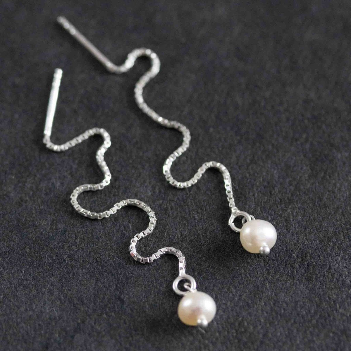 925 Silber Einfädler Ohrringe mit einer kleinen, weißen Perle am Abschluss auf schwarzem Untergrund.