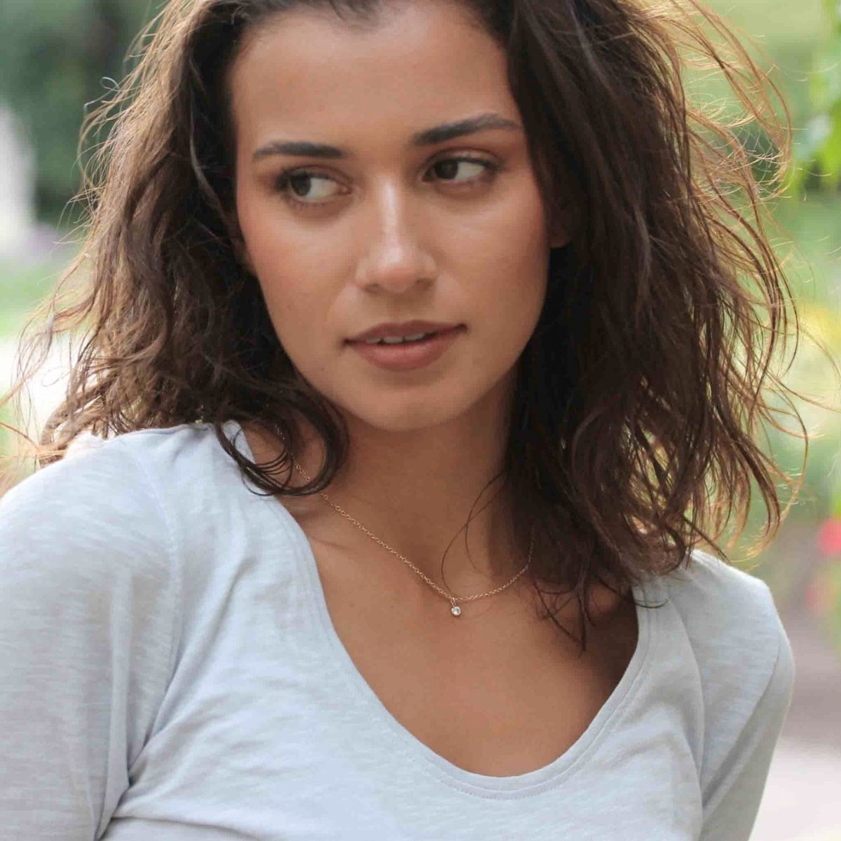 Eine feine Goldkette mit einem winzigen, runden Zirkonia-Anhänger am Hals des Models.