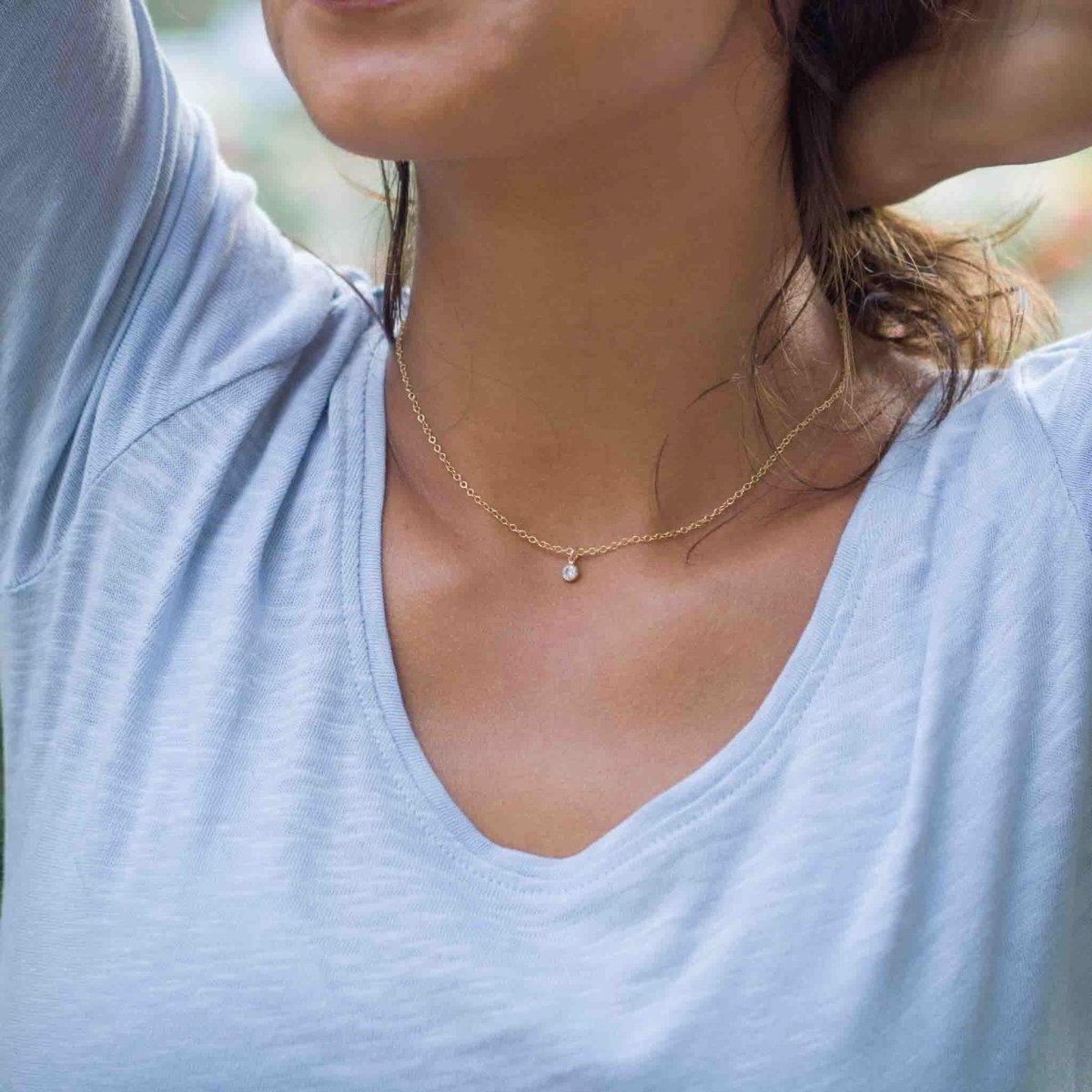 Eine feine Goldkette mit einem winzigen, runden Zirkonia-Anhänger am Hals des Models.