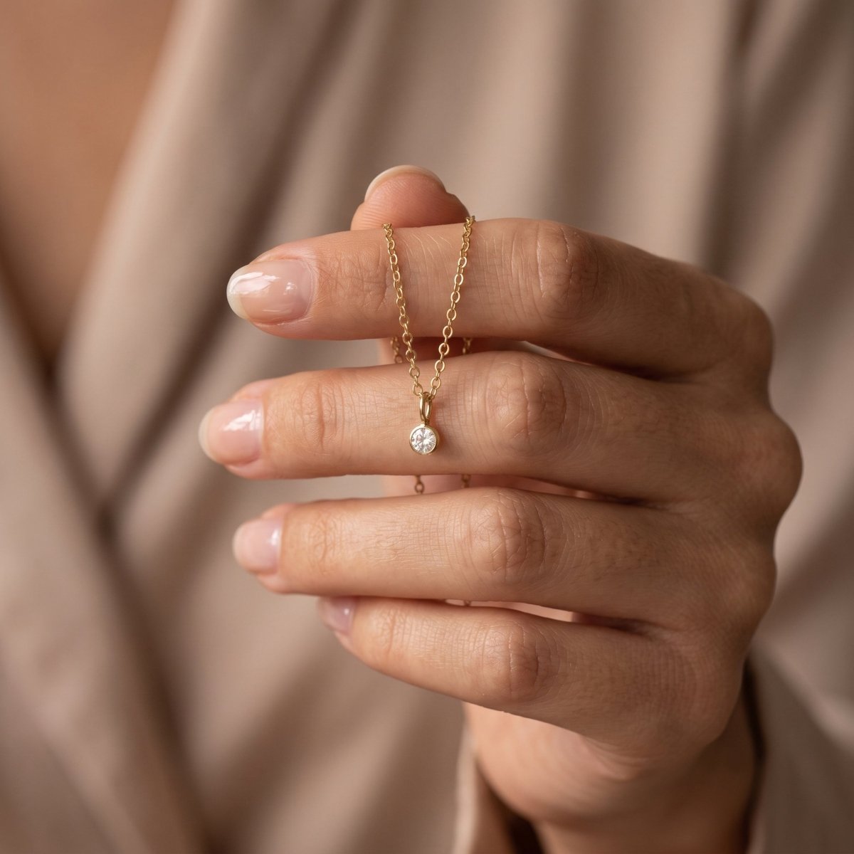 dünne goldkette mit winzigem, rundem zirkonia-anhänger von hand gehalten.