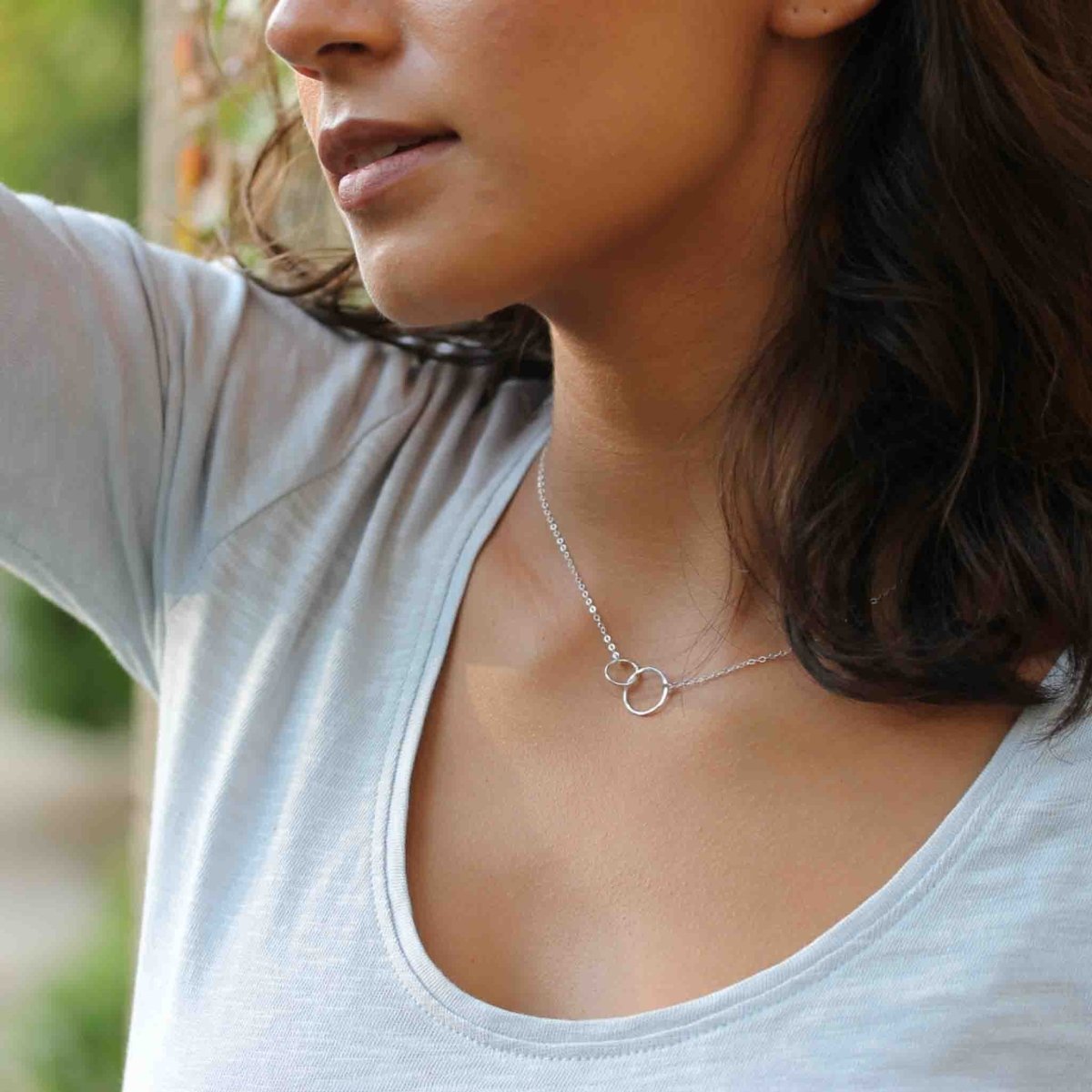 Eine halsnahe Silberkette mit zwei verschlungenen Ringen als Verbinder in der Mitte hängt vom Hals des Models | MAYAMBERLIN